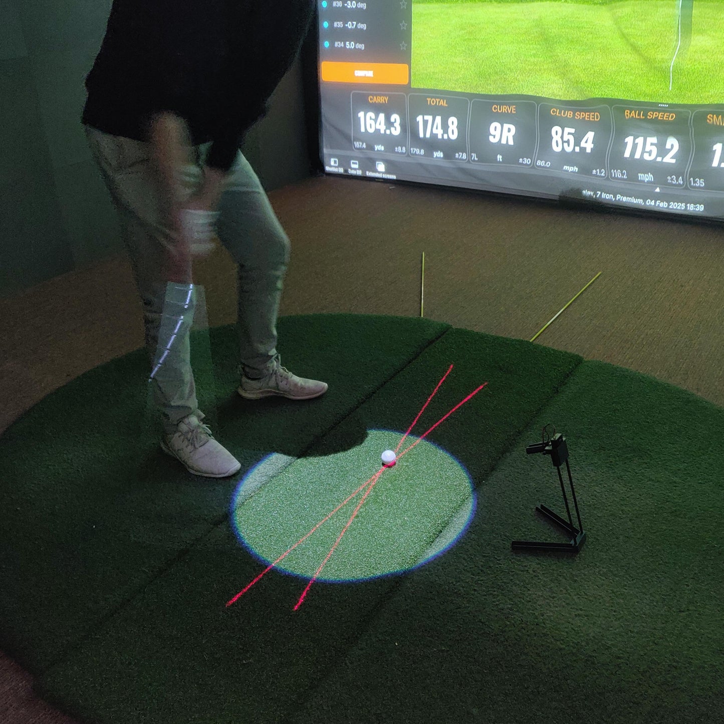 Person playing golf simulation game on a green mat with screen displaying game details.