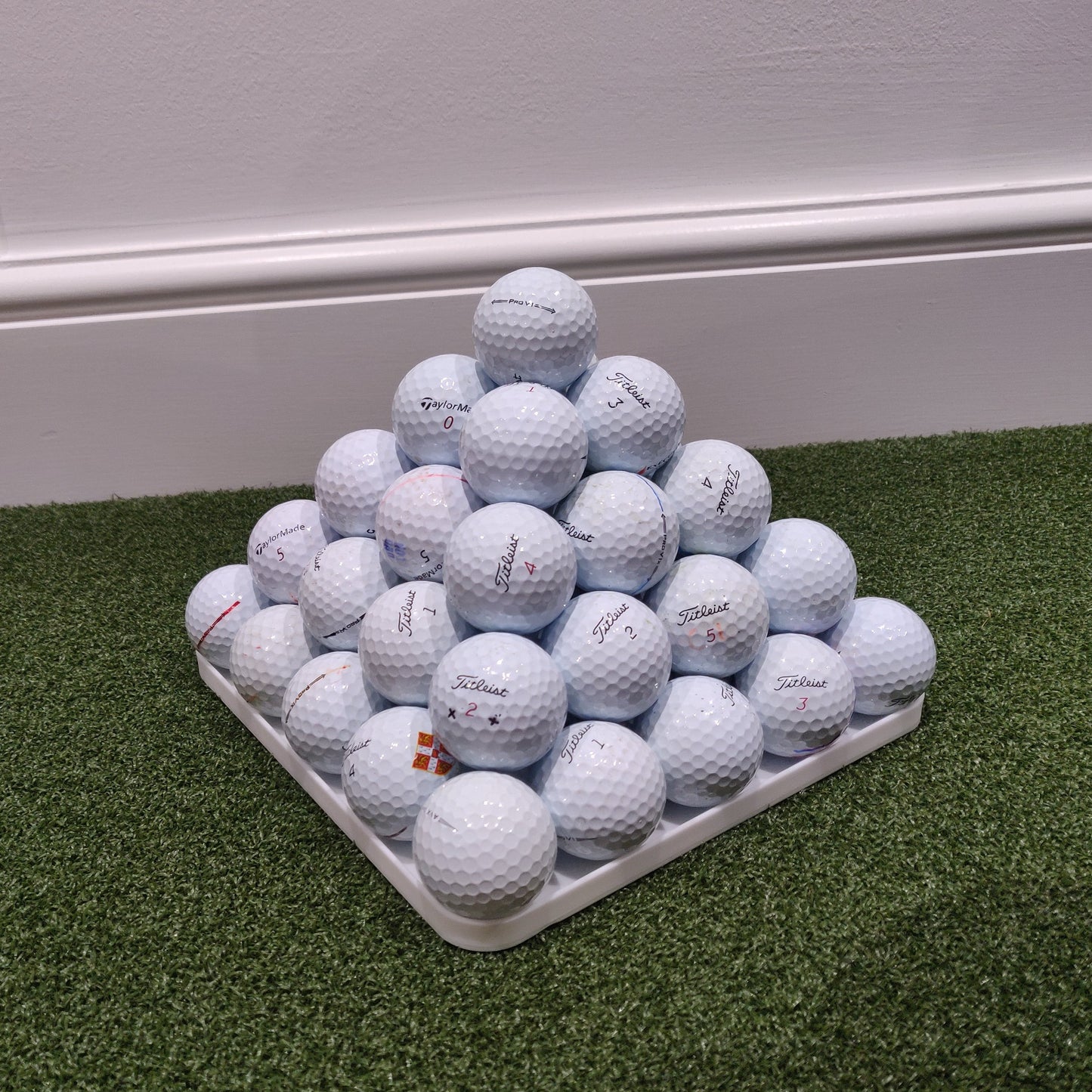 Pyramid of golf balls on a green mat with a white background