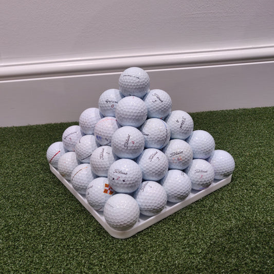 Pyramid of golf balls on a green mat with a white background